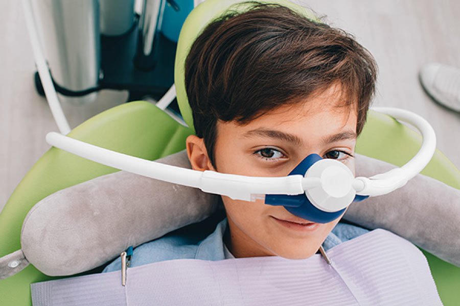 Photo of a brunette boy in the dental chair with a nitrous oxide mask over his nose.
